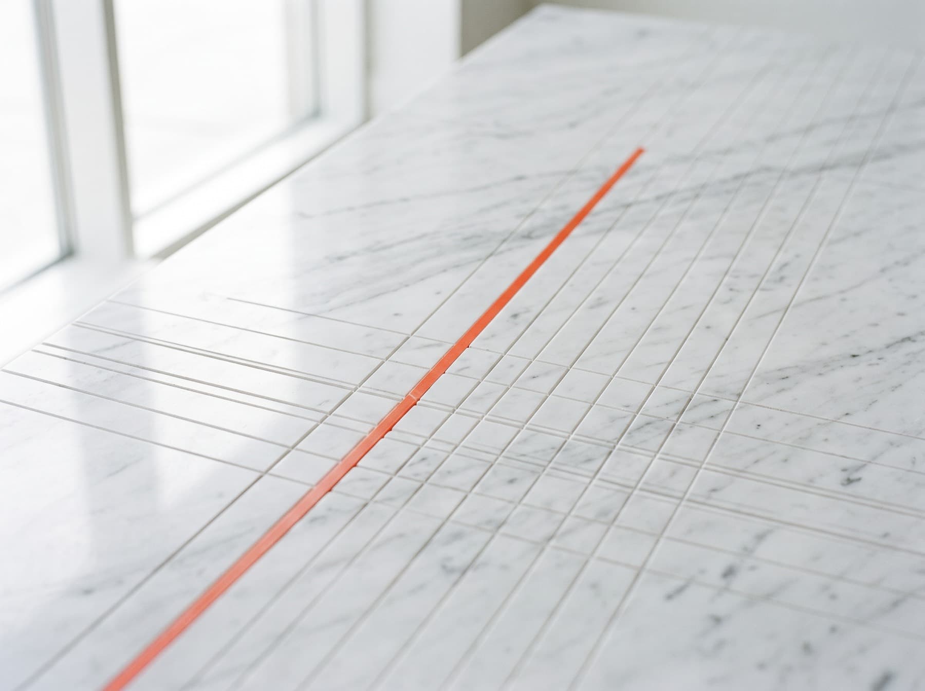 White marble surface with a precise engraved grid and a single orange inlaid line