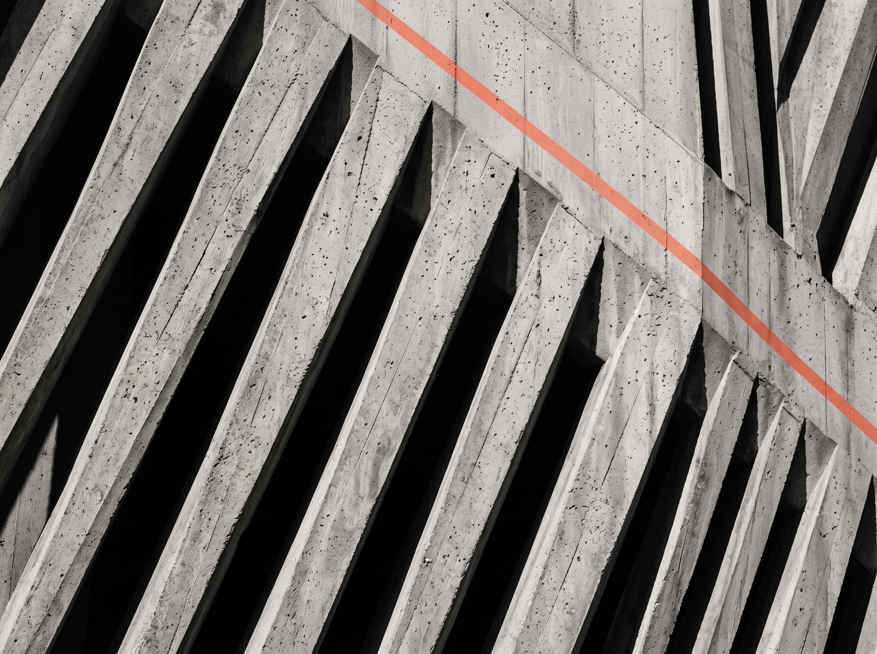 Brutalist concrete wall of angular diagonal ribs with deep shadows, crossed by a thin orange line